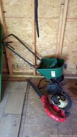 Green Scotts broadcast spreader and red Homelite blower placed on shed floor, showing full units