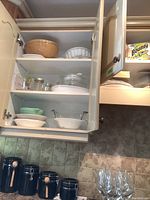 Kitchen cupboard open showing various ceramic casseroles and mixing bowls including a large beige bowl and white patterned bowl.