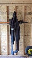 Full front view of the brown Northern Escape chest waders with attached rubber boots hanging from wooden wall.