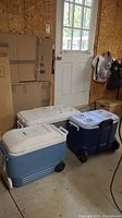 Three coolers lined up in a workshop garage setting against a wall and window, showing different sizes and colors