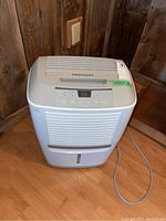 Full view of the white Frigidaire portable dehumidifier sitting on a wooden floor.