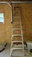Full view of the 8-foot aluminum A-frame step ladder standing upright against a wall in a garage with OSB board paneling.
