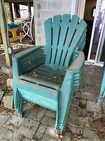Stack of six green resin plastic lawn chairs with dirt and debris on seats and backs, showing outdoor wear.