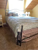 Photo of fully made metal bed with bedding and pillows in a bedroom with tan walls and carpet.