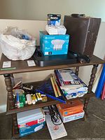 Overview of the office supply lot on wooden table, including paper cutter, light bulbs, glue, rulers, folders, and boxes of envelopes.