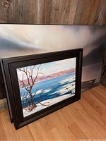 Both framed painting and plaque-mounted print leaning against wood wall