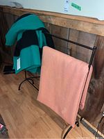 Black metal quilt rack with two blankets draped: green with black stripes Hudson’s Bay label and orange unlabeled wool blanket.