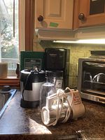 Overview of lot on kitchen counter including coffee maker, compost caddy, Nutri Ninja base with cups, and hand mixer.