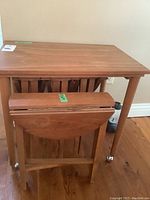 Photo showing teak rectangular nesting table with four folding round tables stored inside, visible from front.