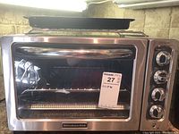 Front view showing stainless steel KitchenAid toaster oven with included rack and baking pans on top.