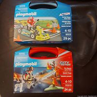 Both Playmobil sets in their original blue and red carry case boxes, showing front packaging with age recommendations and piece counts.