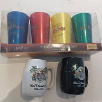 Four plastic Harry Potter tumblers in original packaging and two ceramic Walt Disney World Rainforest Cafe mugs displayed side by side.