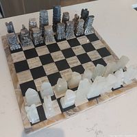 Full view of the marble chess board set-up with all pieces in place showing the contrasting light and dark marble pieces and checkered marble board.