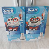 Two sealed boxes of Oral-B rechargeable toothbrushes for kids showing front packaging with cartoon tooth character and product features.