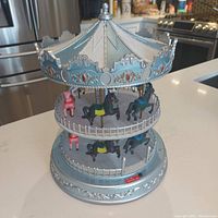 Full view of the blue and silver two-tier Christmas-themed musical carousel with horses and decorative accents