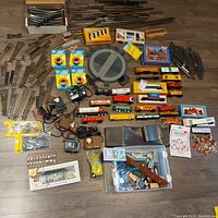 Wide view of the lot laid out on the floor, showing track sections, turnout switches, transformers, various rolling stock cars, boxes, and miniature figures and accessories.