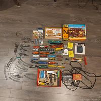 Overview of lot showing multiple rolling stock cars in colors like orange, red, blue, green arranged alongside track pieces, transformers, remote switches, and accessory boxes including Pola and Life-Like building kits