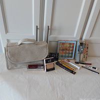 Full lot arranged on white surface showing makeup bag, eyeshadow palette, brush, primers, blush, mascara, lip polish, and eyeliners.