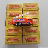 Eleven yellow Matchbox boxes arranged with one fire tender diecast model displayed on top showing the side profile with fire service markings and mounted ladder.