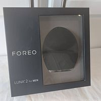 Front view of the black Foreo Luna 2 for Men in its sealed retail box, showing the product through transparent window and branding on the box.