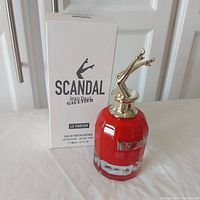 Photo of red faceted perfume bottle with gold legs cap, next to white box with black text reading Scandal Jean Paul Gaultier Le Parfum Intense 80ml tester.