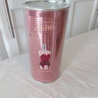 Front view of the cylindrical metallic pink tin container with Jean Paul Gaultier Classique perfume branding and bottle image.