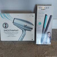 Box of Conair InfinitiPro Smoothwrap hair dryer and box of Conair Boutique 1 inch hair straightener shown together on floor.