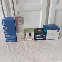 Photo showing five boxed skincare products in a row on a white surface against a door background.