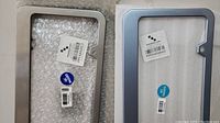 Close-up of two new North American size license plate frames in silver and light blue with installed quality assurance and product code stickers.
