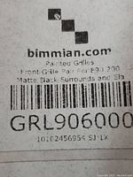 Close-up of box label from bimmian.com indicating front grille pair for BMW E90 200 with matte black surrounds and slats, item code GRL906000.