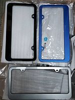 Three painted glass license plate frames in black, blue and silver arranged together on bubble wrap.