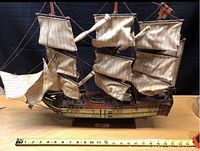 Full side view of wooden model ship with fabric sails and measuring tape showing approximate size of 24 inches.