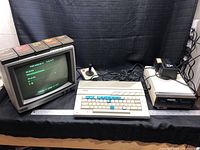 Full setup showing computer, monitor, drive, joystick, game cartridges on top of monitor and power supplies