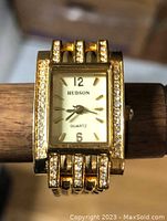 Hudson ladies quartz watch with crystal trim and rectangular face shown on a wood stand.