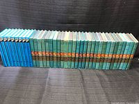 Full view of the large lot of Hardy Boys books showing blue, teal, and brown spine books arranged in two groupings horizontally.