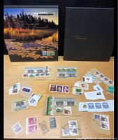 Wide view showing the hardcover Collection Canada stamp album and various loose arranged Canadian stamps on paper.