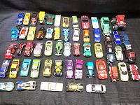 Top down view of 47 assorted die-cast and plastic toy cars arranged in rows by color and type including race cars and trucks.