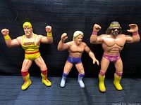 Three WWF wrestling figures standing side by side against black fabric background showing full frontal view of each figure.