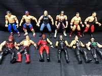 Full lot of 12 WWF wrestling action figures laid out on a black fabric background, showing diverse characters and attire.
