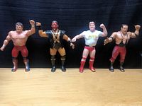 Four vintage wrestling action figures standing side by side on a wooden surface against a black background.