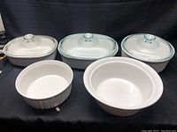 Full view of 5 CorningWare white stoneware cookware pieces, 3 with lids and 2 without.