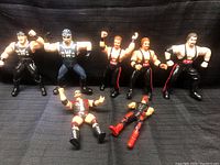 Overview of all seven nWo wrestling figures laid out on black cloth, showing standing and lying poses.