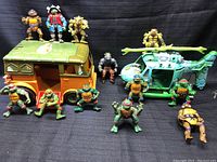 Front and side view showing several Teenage Mutant Ninja Turtles action figures with the Turtle Van and helicopter vehicles in background.