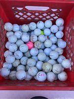Top view of red milk crate filled halfway with white golf balls showing some dirt and wear.