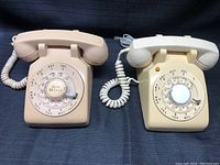 Pair of vintage rotary desk phones side by side showing front view with rotary dials and handsets resting on top