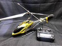 Photo of yellow and black remote control helicopter with dual rotors alongside its radio controller