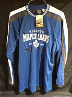 Full view of blue long sleeve Toronto Maple Leafs shirt showing front design and colors.
