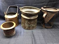 Four vintage copper kitchen items on dark cloth background, kettle, two pots, and wire mesh strainer.