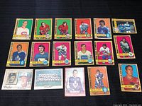 Top view of 19 vintage hockey cards spread on black surface showing player portraits, colorful borders, team names, and logos.