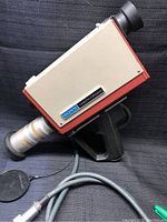 Side view showing boxy design, Sony videocorder label, pistol grip handle, attached long lens, and cable.